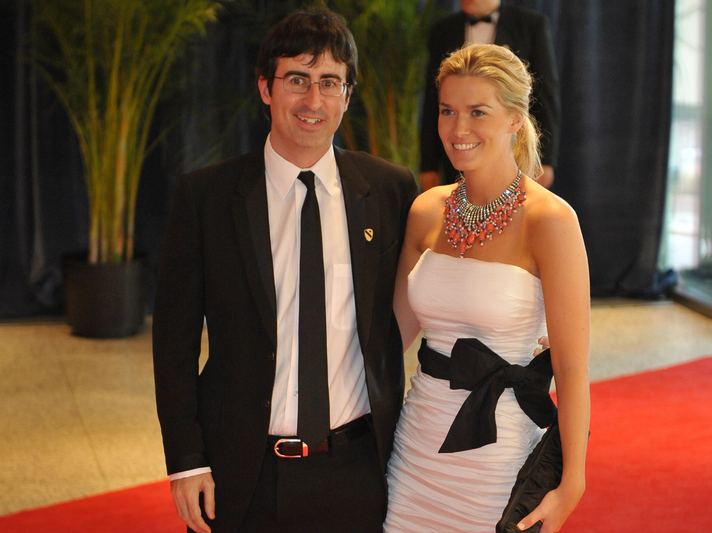John Oliver (L) in black suit and tie with Kate Norley, who is in a white dress with a black belt