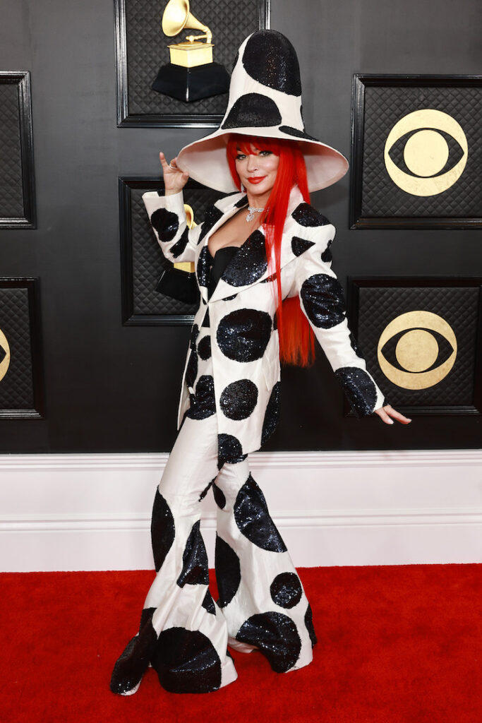 Shania Twain posing on the red carpet in a black and white polka dotted outfit and extremely large hat
