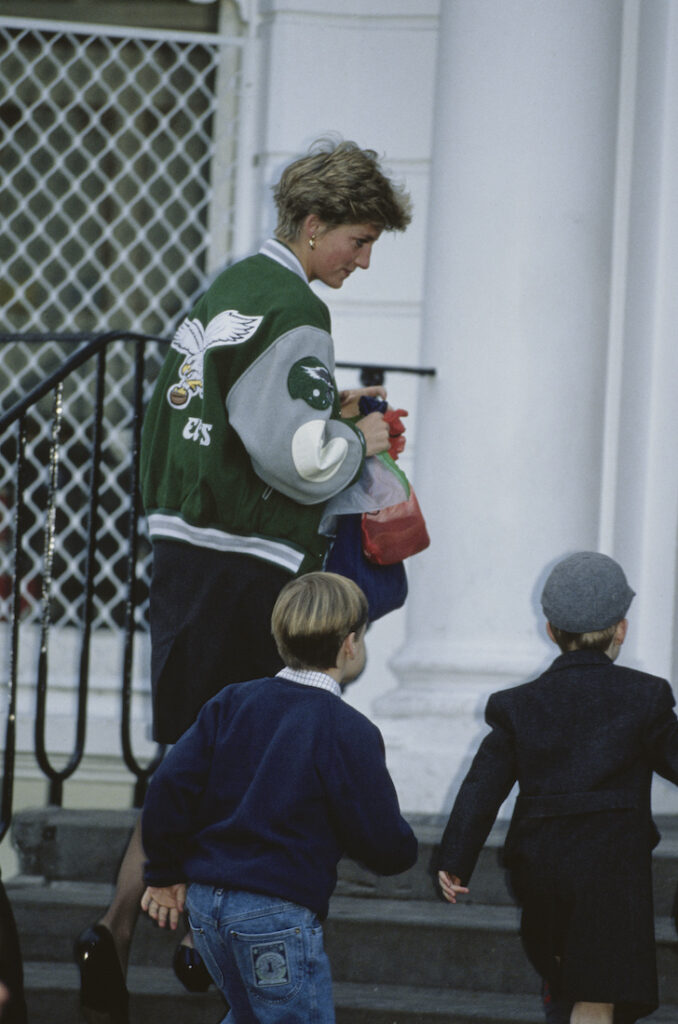 Princess Diana in an Eagles jacket walking her two children up stairs into a school