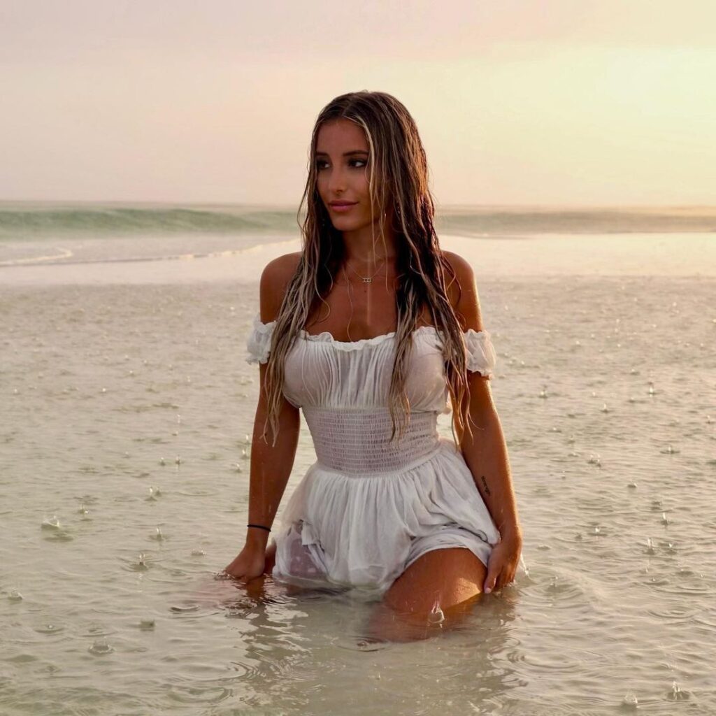 Hannah Kotick takes a dip in the sea while wearing a short white dress.